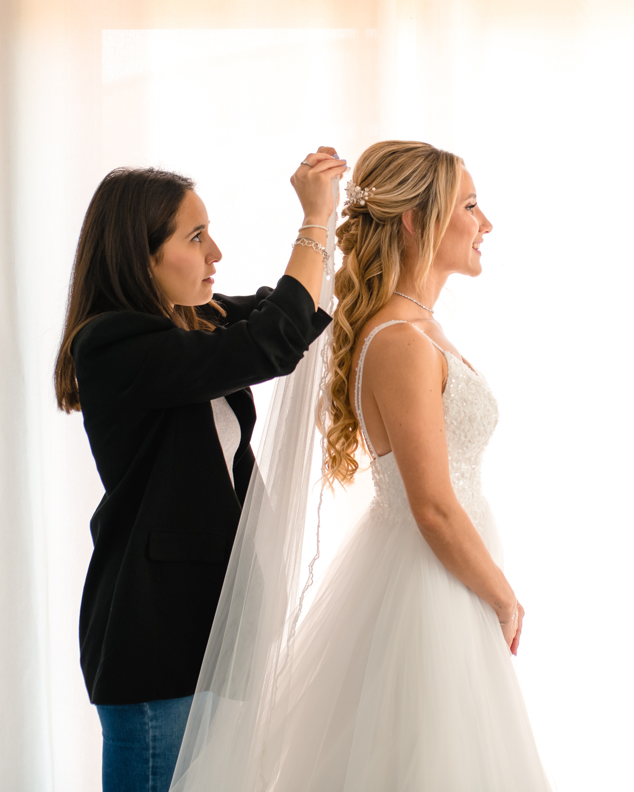 Maquilladora ajustando el peinado de una novia con ondas y velo durante la preparación de boda en Barcelona