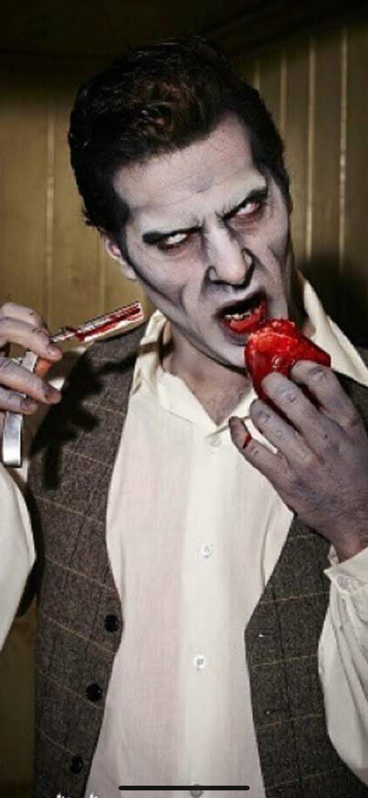 Hombre con maquillaje Halloween profesional de estilo zombi, piel pálida, ojos oscurecidos y sangre ficticia alrededor de la boca.